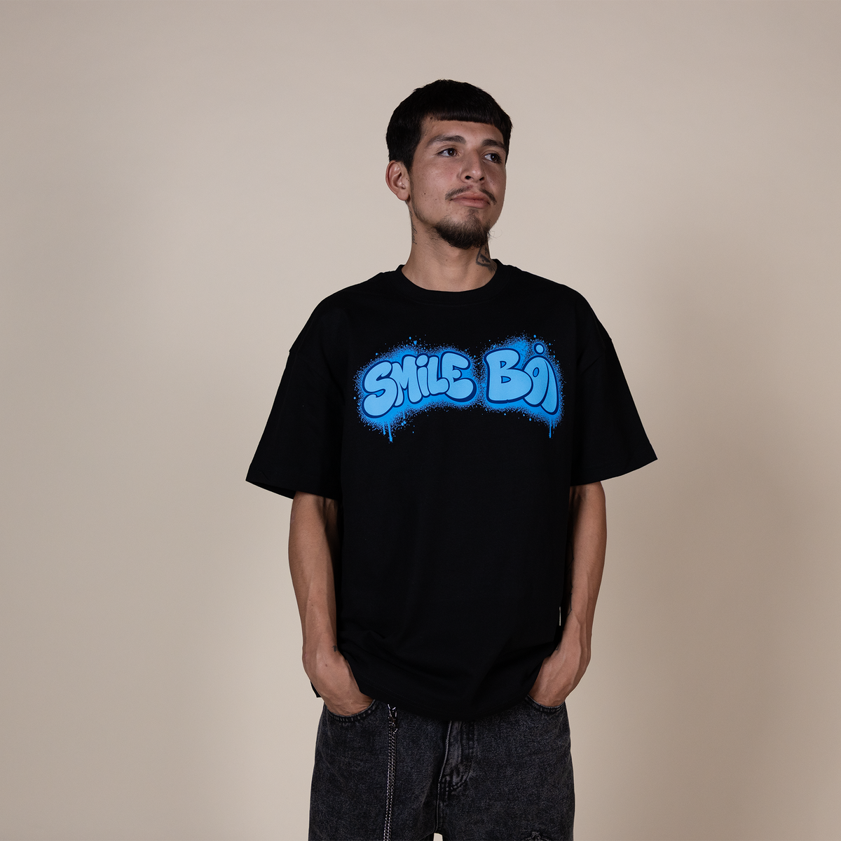 A man wearing a black t-shirt with a blue 'SMILE BOY' graphic, standing against a plain beige background.